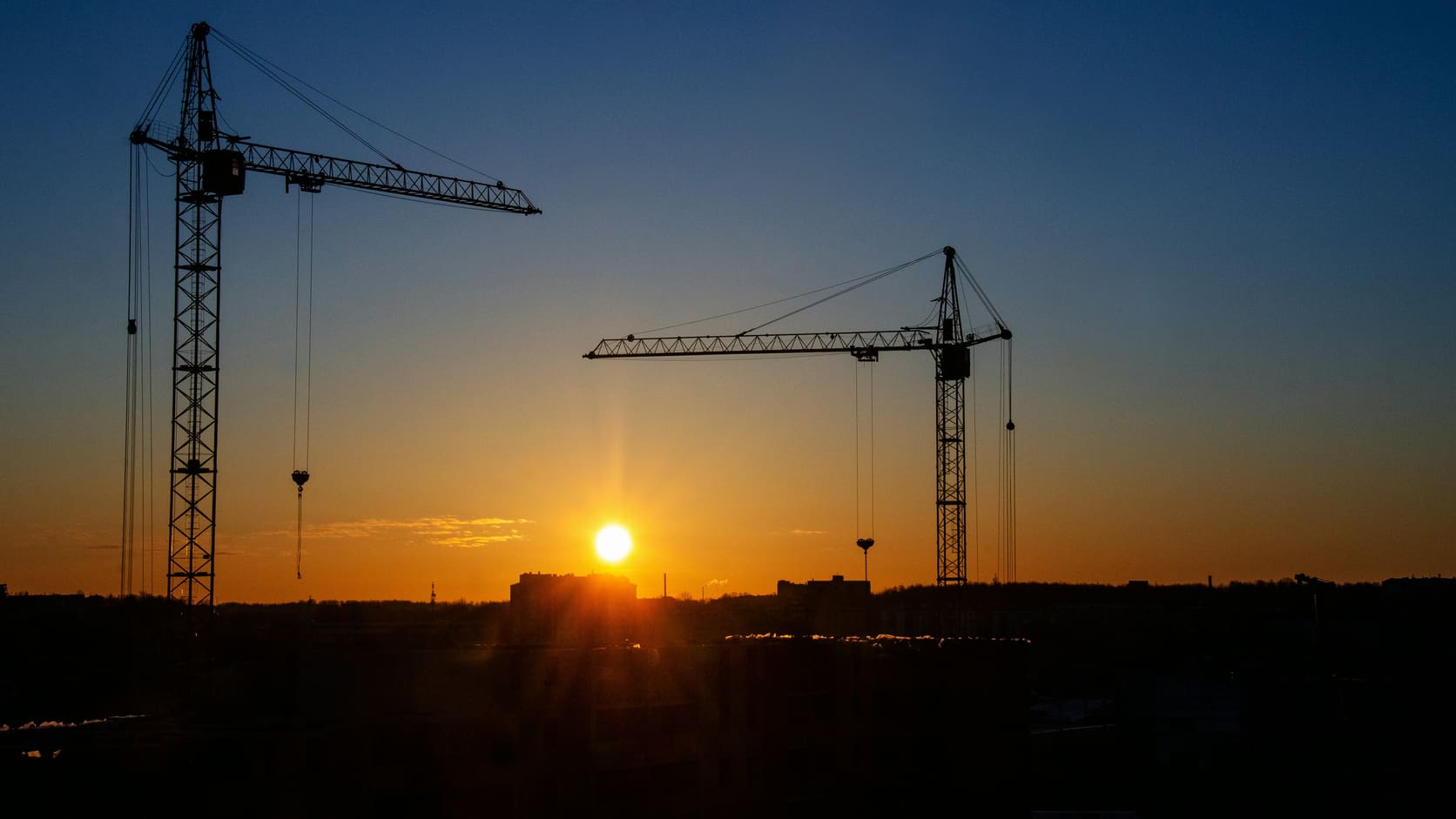Illustrative silhouette of two construction cranes against a sunset sky
